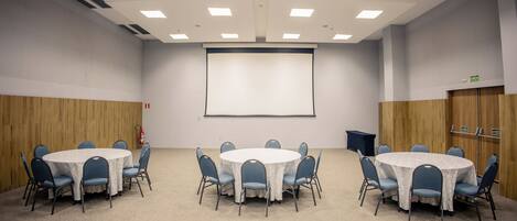 A conference room with a white table, blue chairs, a projector screen, and a whiteboard.