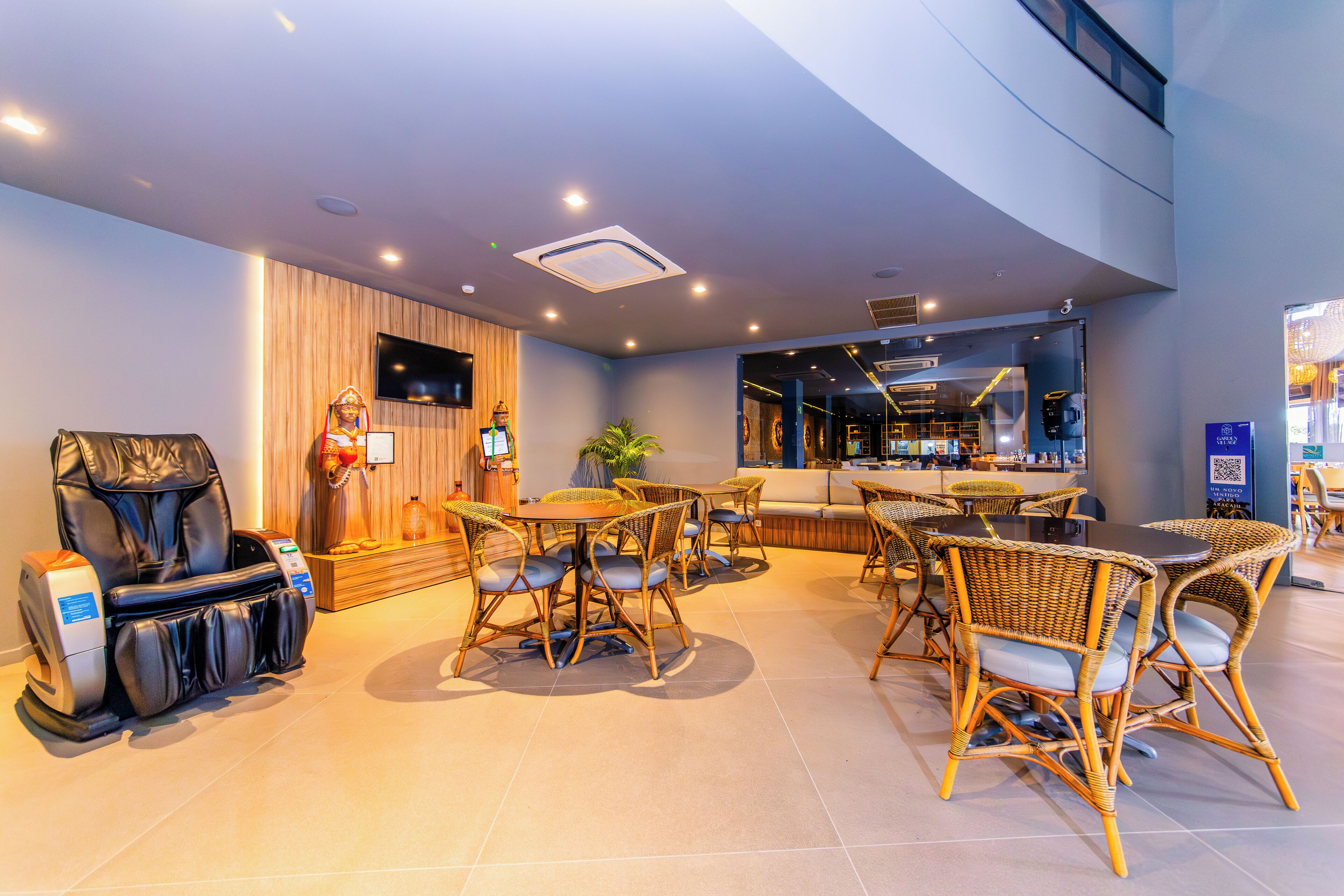 A modern hotel lobby with a massage chair, wicker furniture, and a bar area.
