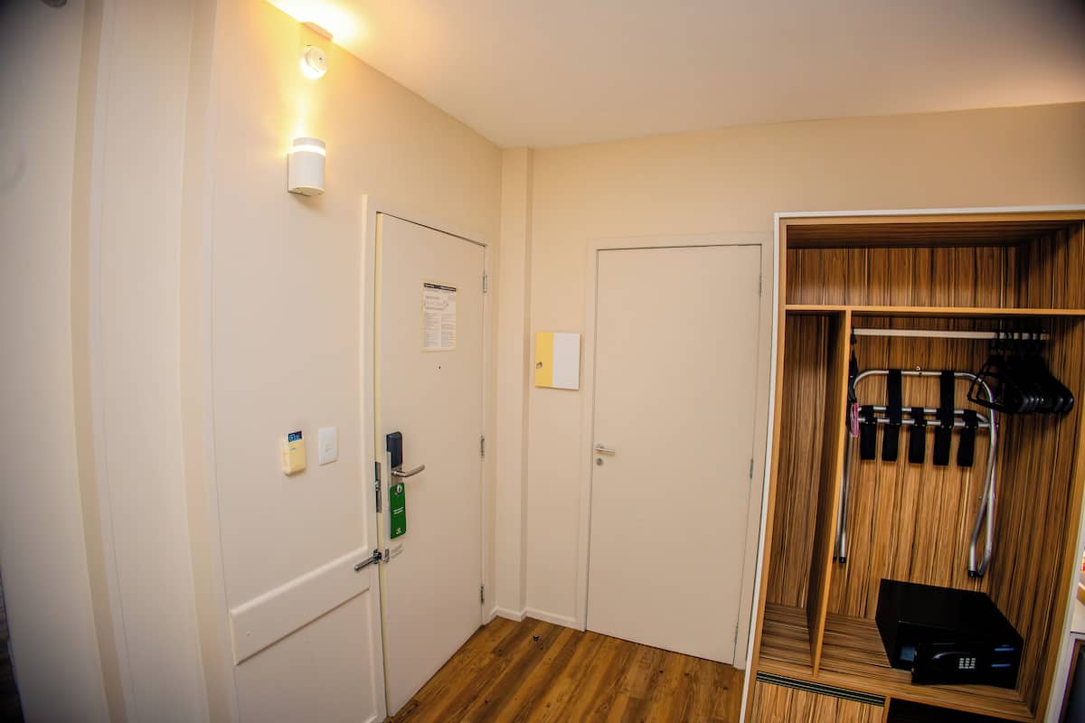 Een hotelkamer met een houten vloer, een kast met hangende kleding en een deur met lichtschakelaar en slot.