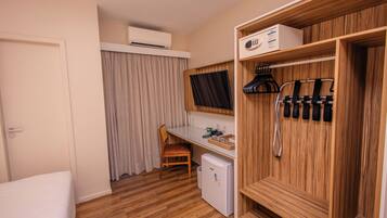 A compact room with a bed, a desk, a chair, a small refrigerator, a wardrobe, and a window with curtains.