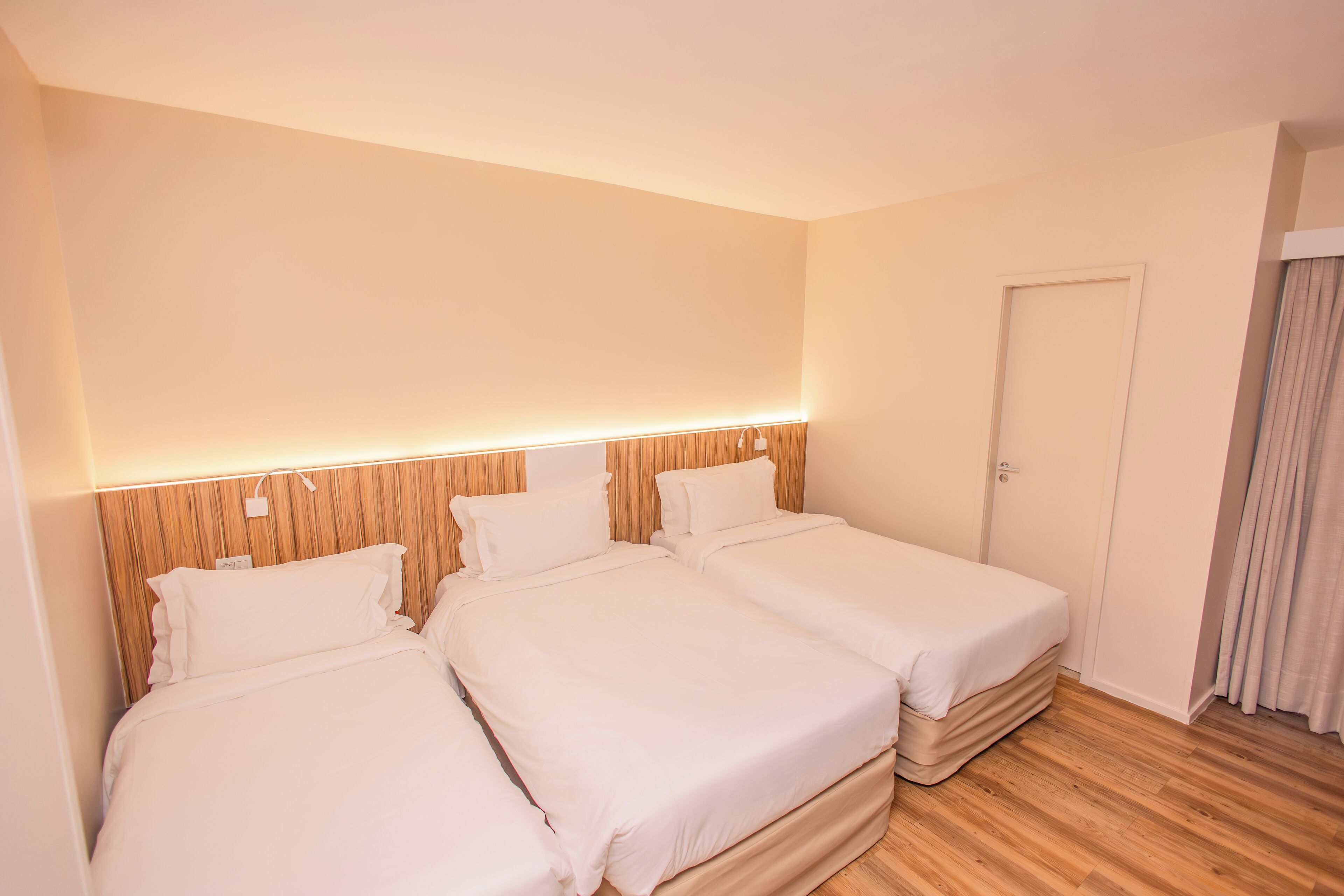 A hotel room with two single beds, wooden headboard, and a door with a curtain.