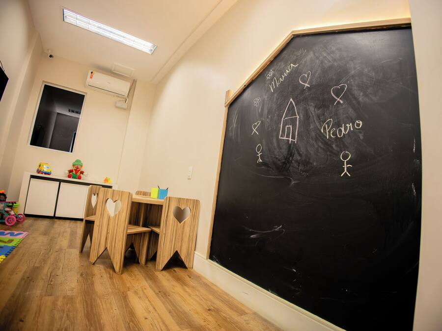 Un aula con una pizarra, sillas de madera, un escritorio y un tapete de juego colorido.