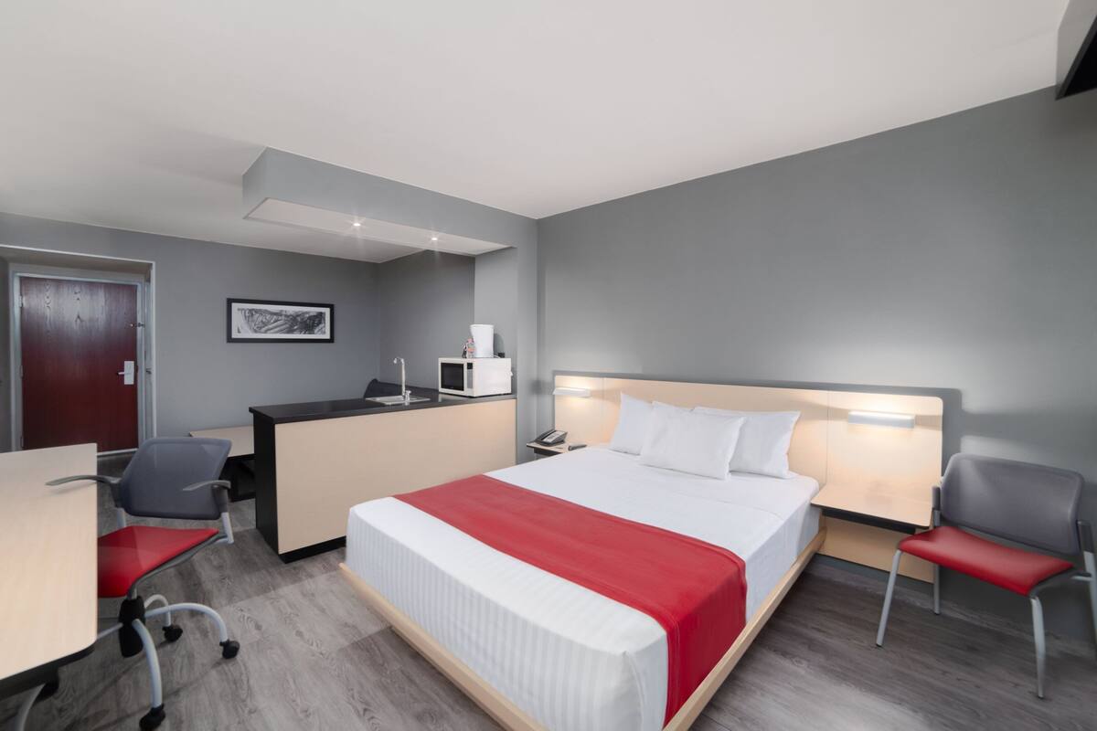 A hotel room with a bed, desk, chairs, and a microwave.