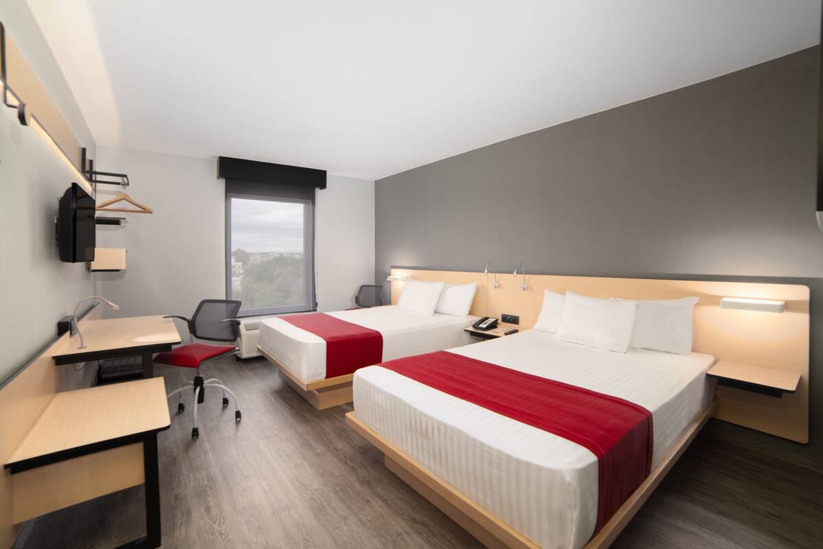 A hotel room with two beds, a desk, a chair, a TV, and a window with a view.