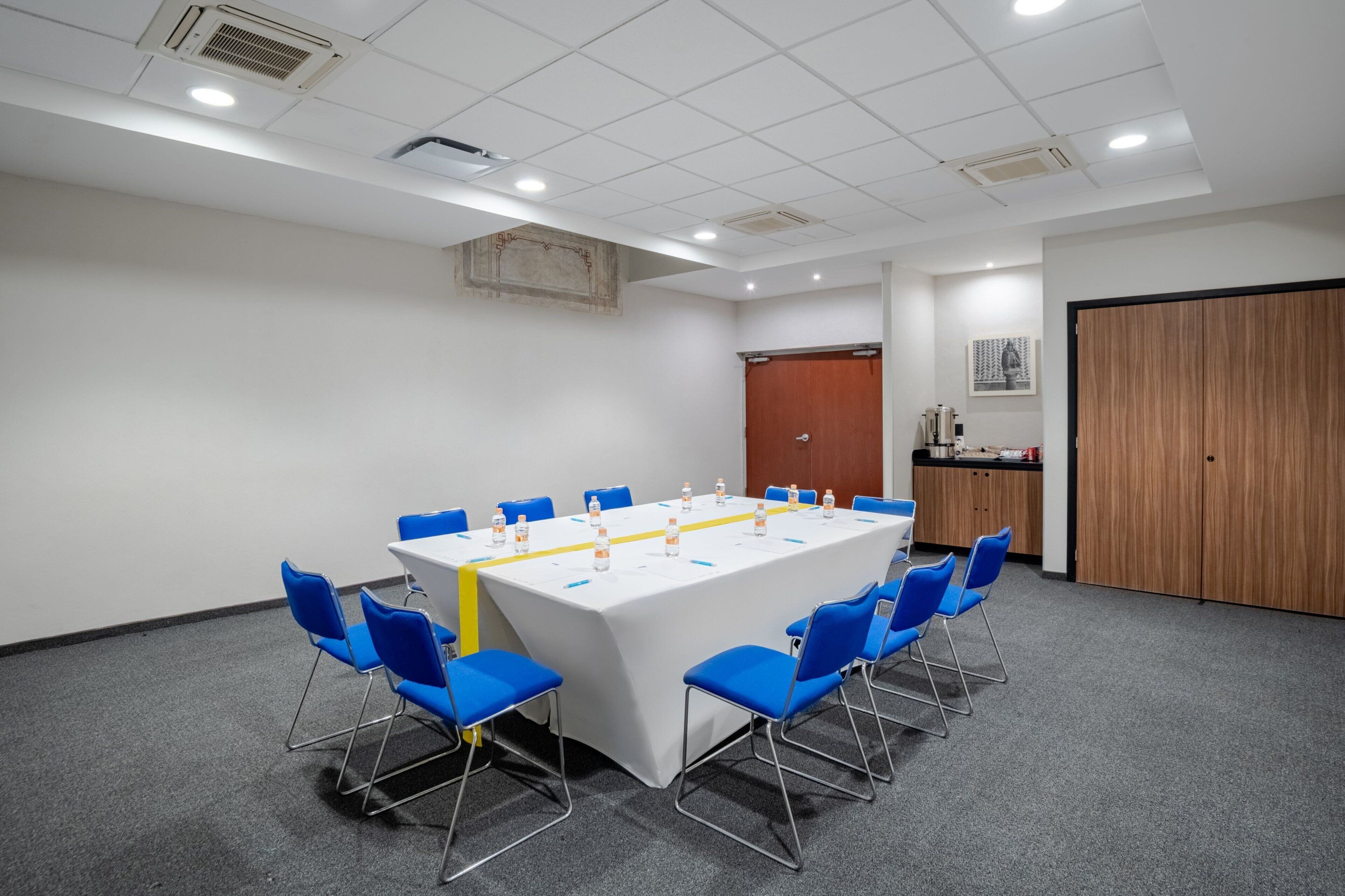 Un salón de conferencias con una larga mesa, sillas azules y un mantel blanco.