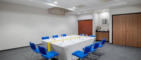 Un salón de conferencias con una larga mesa, sillas azules y un mantel blanco.