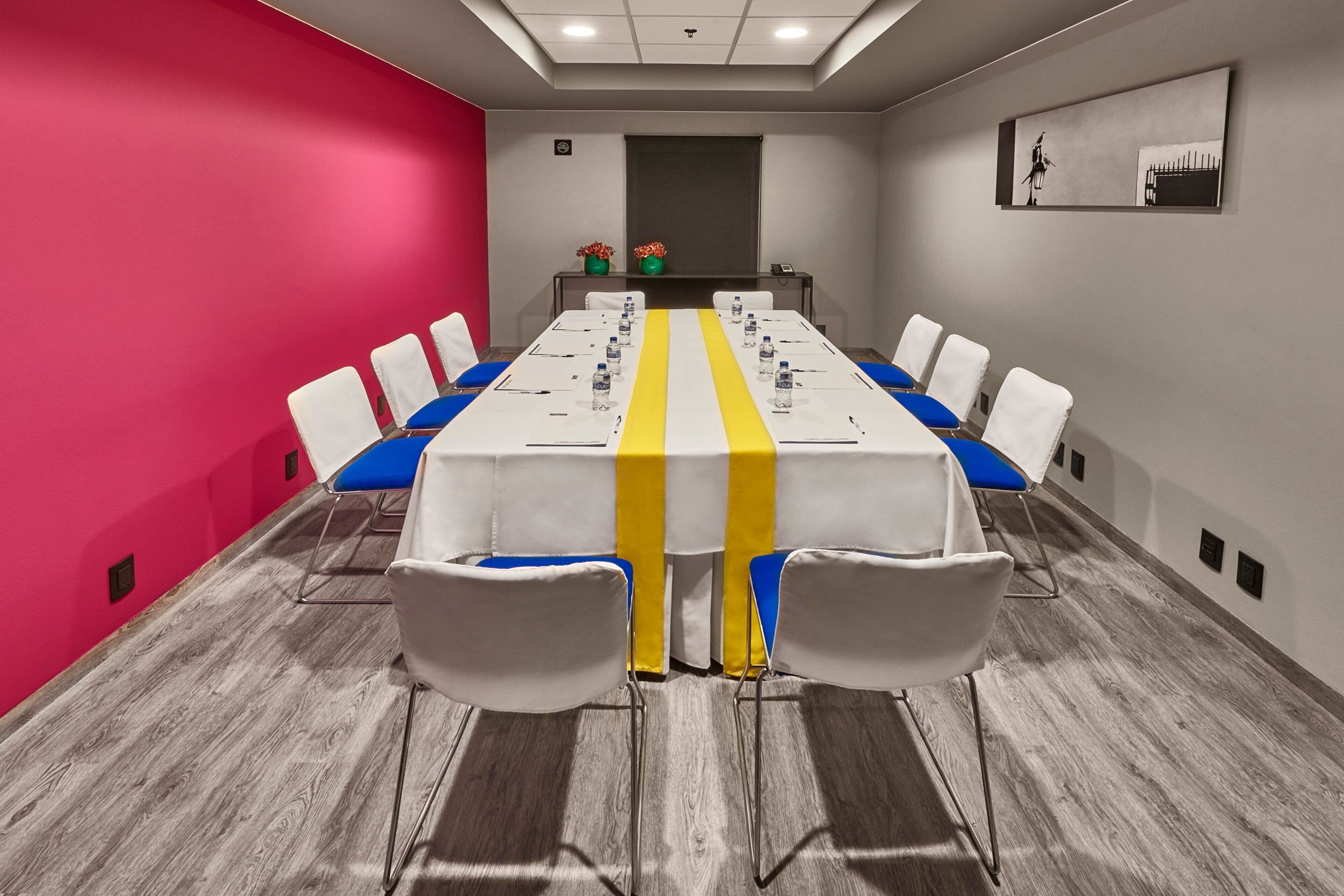 A conference room with a long table, white chairs, and a yellow-striped tablecloth.