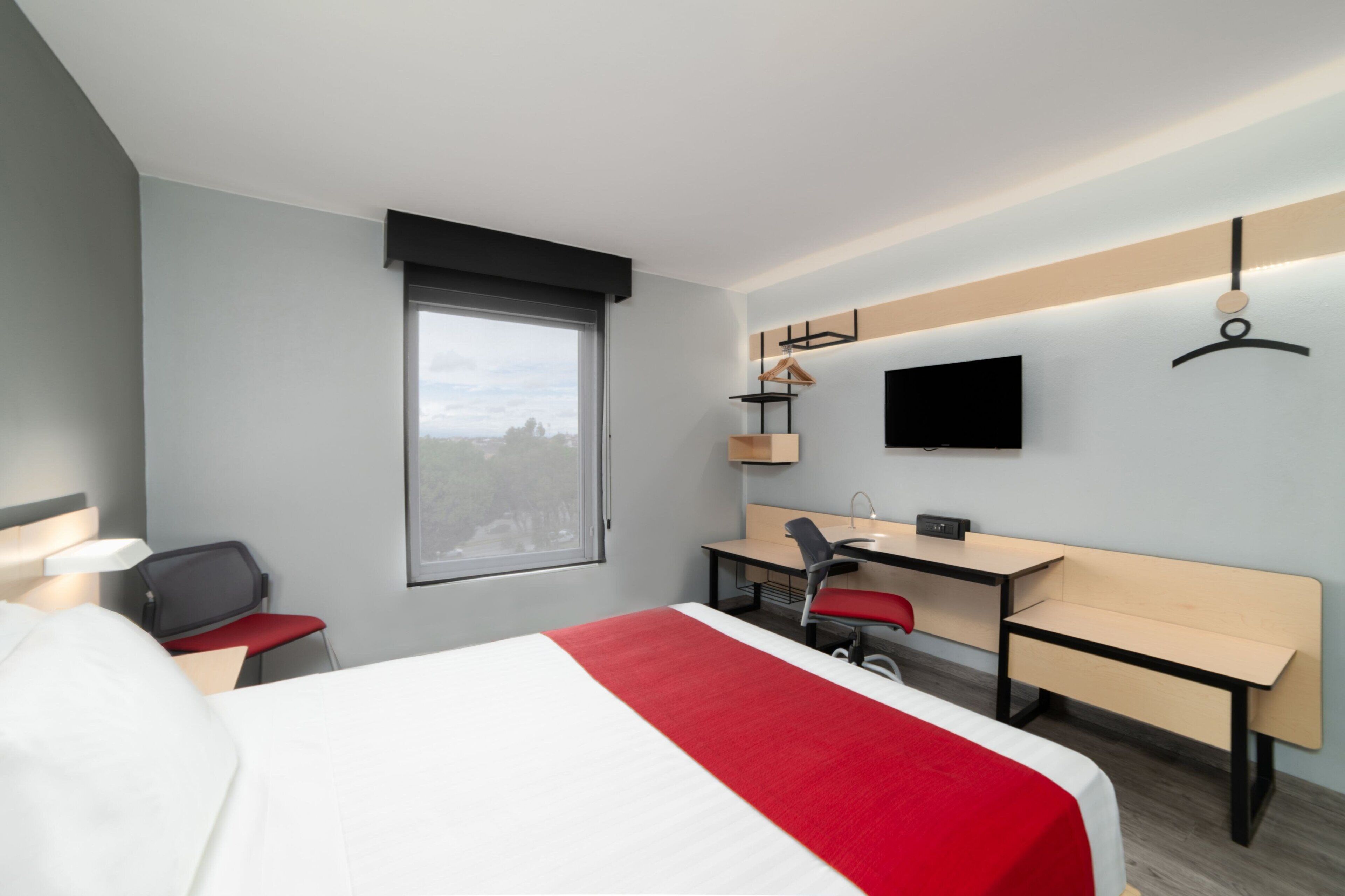 A hotel room with a bed, desk, chair, and a TV mounted on the wall.