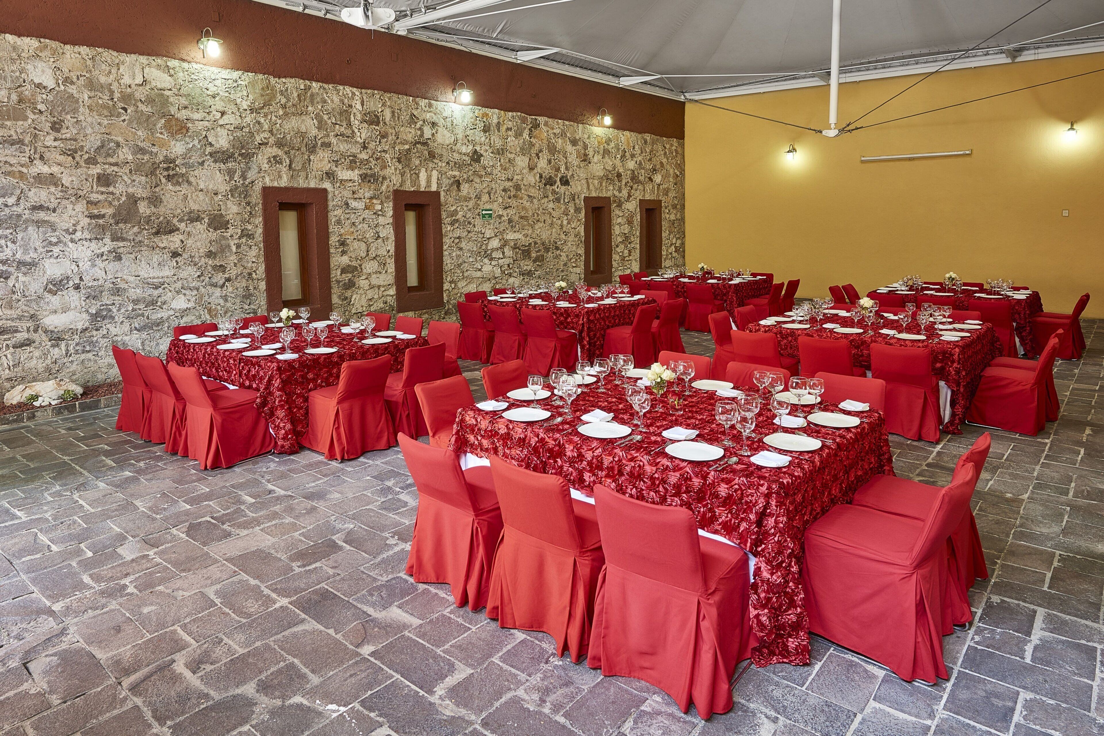 A banquet hall with stone walls, red tablecloths, and matching chairs.