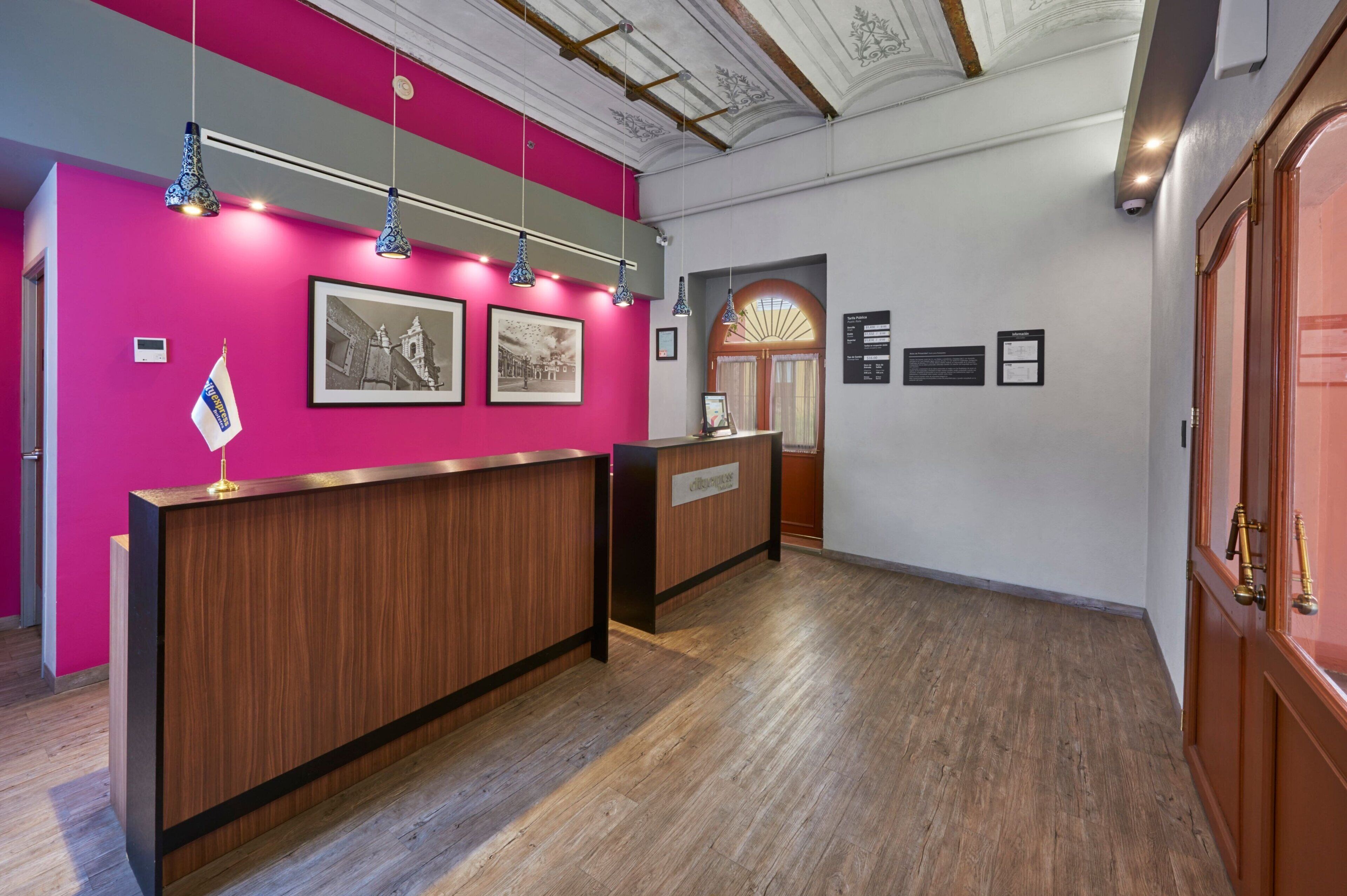 A reception area with a wooden reception desk, a pink wall, and framed pictures.