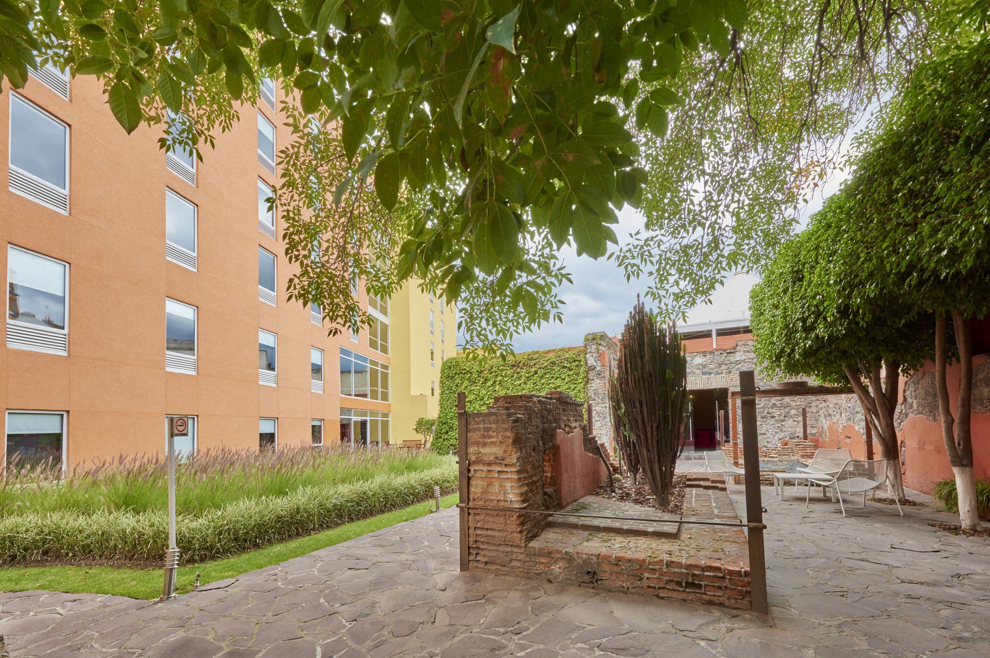 A courtyard with a brick wall, a metal gate, and a building with multiple windows.