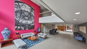 Un hall d’entrée moderne agrémenté d’un grand tableau abstrait, d’un espace détente avec des canapés et une table basse, ainsi que d’un comptoir d’accueil.
