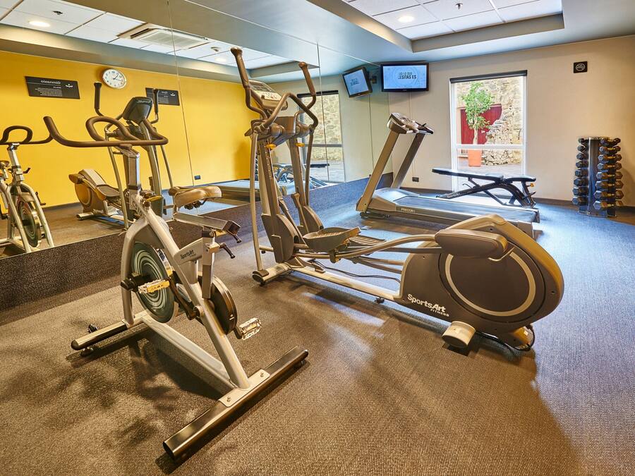 Un gimnasio con máquinas de cardio, pesas y una pantalla de televisión.