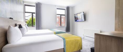 A hotel room with two beds, a TV on the wall, and a view of the city through large windows.