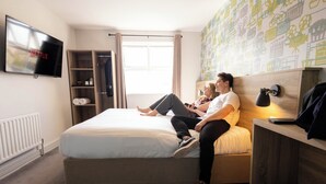 A bedroom with a bed, a TV displaying 'NETFLIX', a wardrobe, and a bedside table with a lamp. - The Camden Hotel (Dublin)