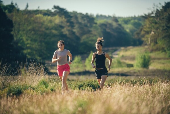 Deux personnes font du jogging dans un champ herbeux, avec des arbres en arrière-plan.