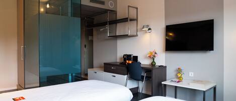 A hotel room with two beds, a desk with a chair, a television, and a small table with a vase of flowers.