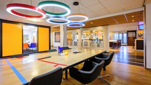 A modern conference room with a long table, black chairs, and colorful ceiling lights. - Hotel Papendal (Arnhem)