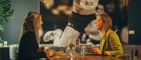Dos personas cenando en una mesa con un cartel decorativo de fondo.