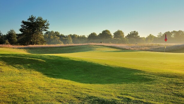 A golf course with a flagstick, trees, and a clear sky. - Hotel Papendal (Arnhem)