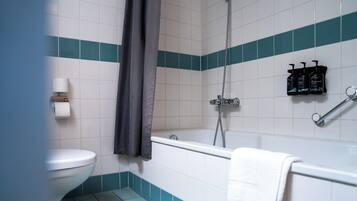 Een badkamer met toilet, bad en douche. Er staan toiletartikelen op de muur.