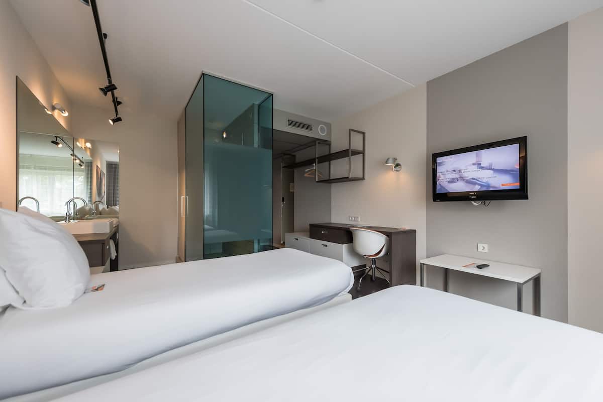 A modern hotel room with a bed, a desk, a TV, and a bathroom.