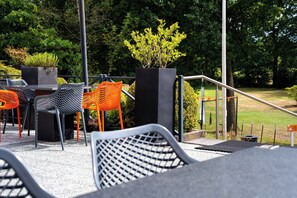 Outdoor seating with chairs and tables, surrounded by greenery and a metal railing. - Hotel Papendal (Arnhem)