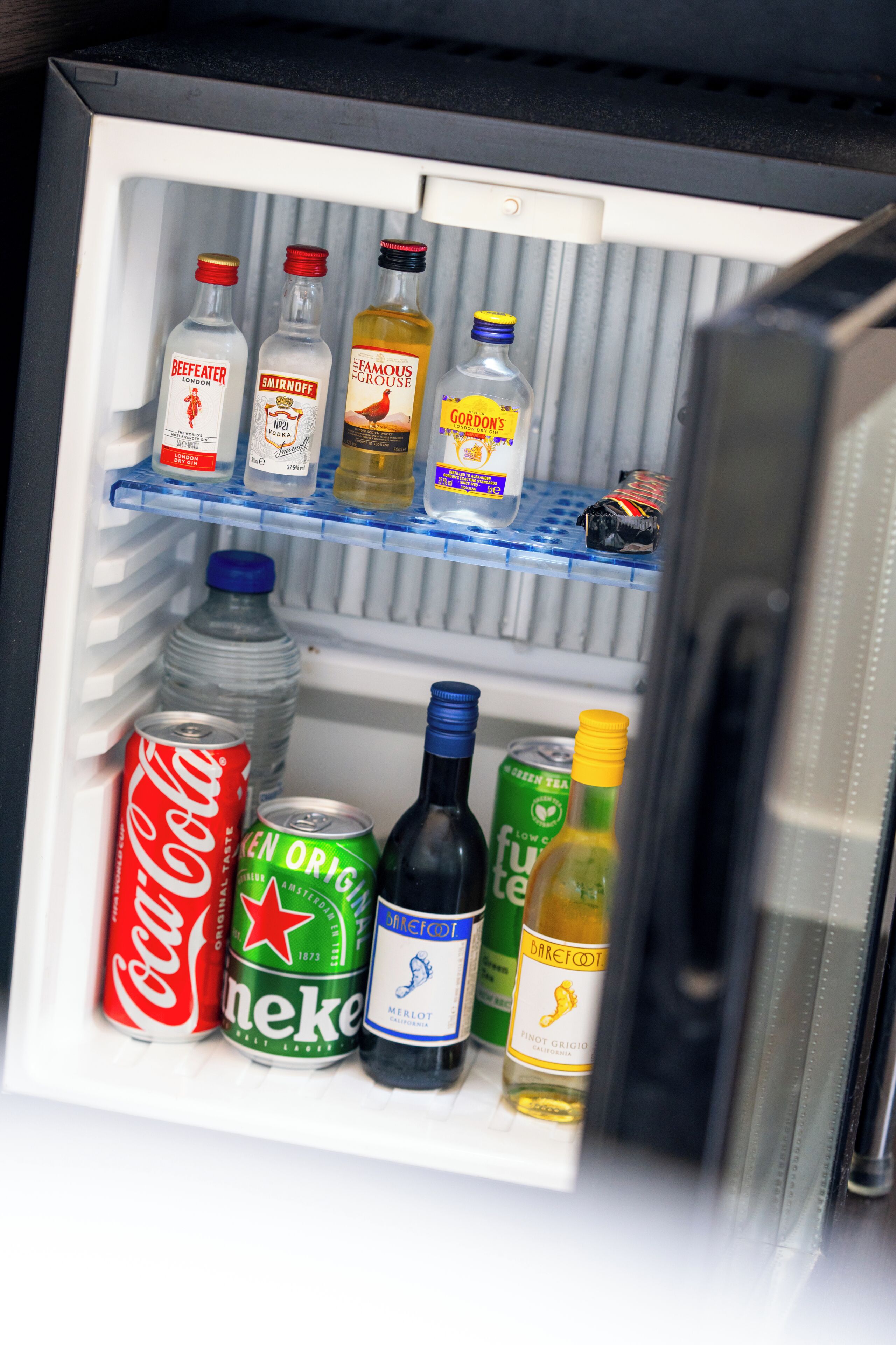 A refrigerator containing various beverages including bottles of gin, beer, and soda.