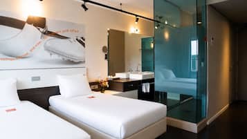 Une chambre d’hôtel moderne avec deux lits, un grand miroir, une cloison en verre et une œuvre d’art accrochée au mur.