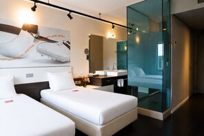 A modern hotel room with two beds, a large mirror, a glass partition, and a wall-mounted artwork. - Hotel Papendal (Arnhem)