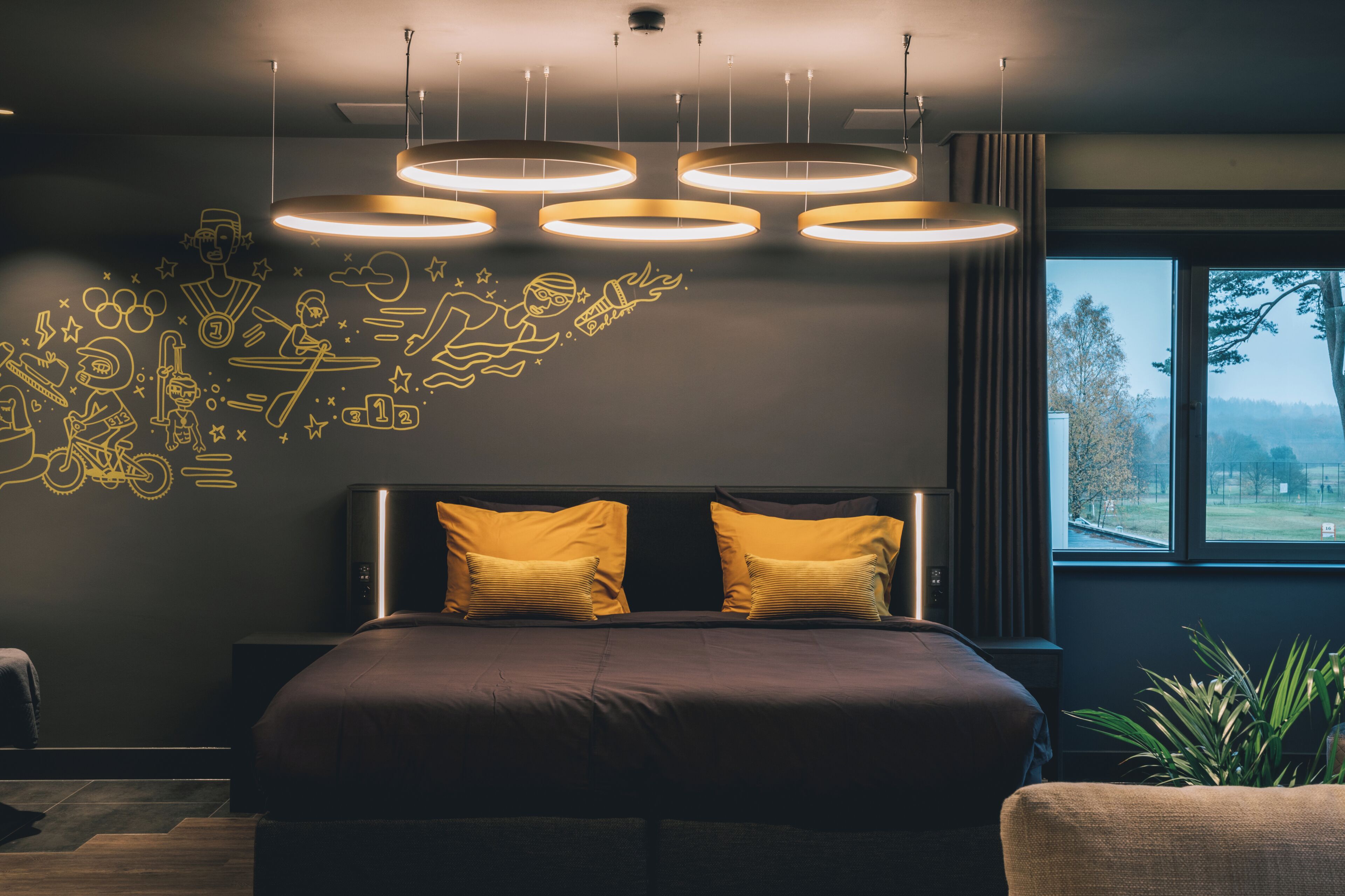 A modern bedroom with a large bed, a headboard with two pillows, and a wall with doodle-style drawings.