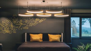 A modern bedroom with a large bed, a headboard with two pillows, and a wall with doodle-style drawings. - Hotel Papendal (Arnhem)