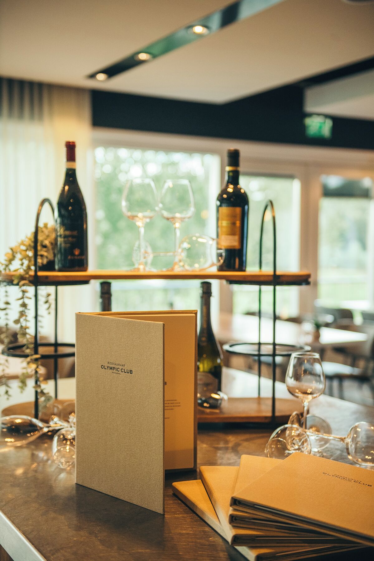 En restaurantindretning med barområde, vinglas, flasker og en menustativ.