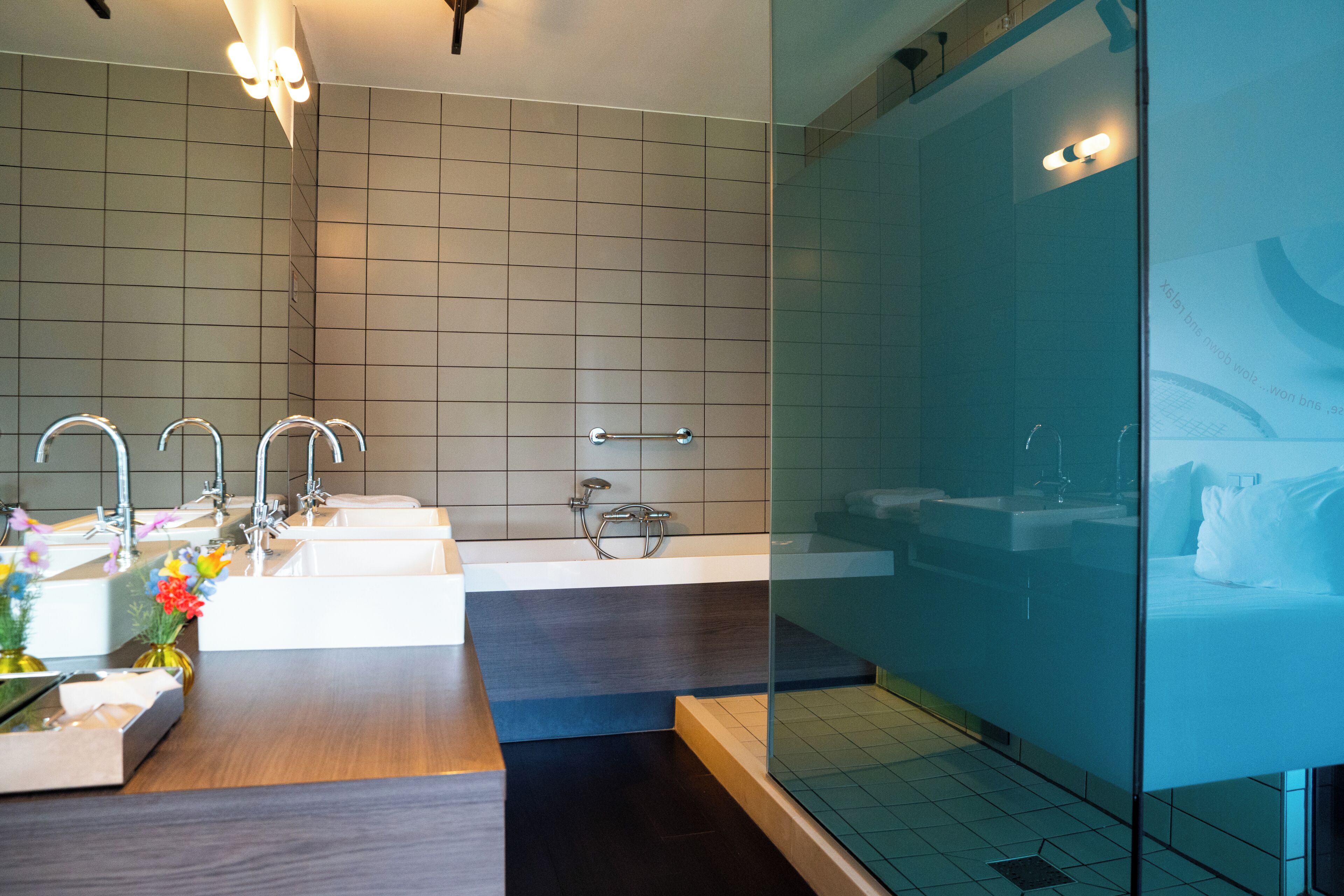 Un baño moderno con cabina de ducha de vidrio, tocador de madera con dos lavamanos y un perchero para toallas.