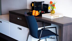 A modern office desk with a coffee maker, two orange mugs, a vase with flowers, and a book titled 'Moments'. - Hotel Papendal (Arnhem)