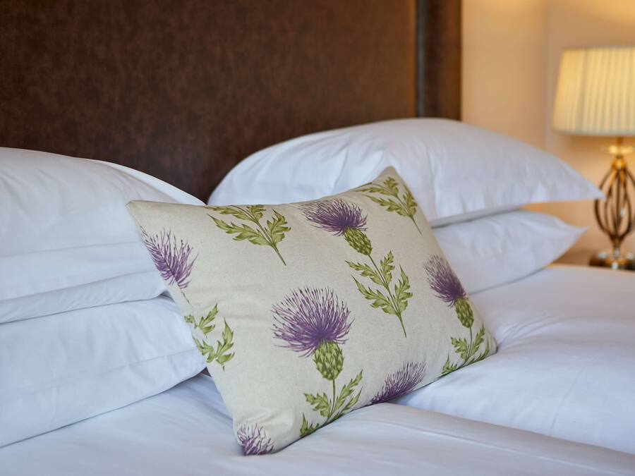 A neatly made bed with white linens and a decorative pillow featuring a floral pattern.