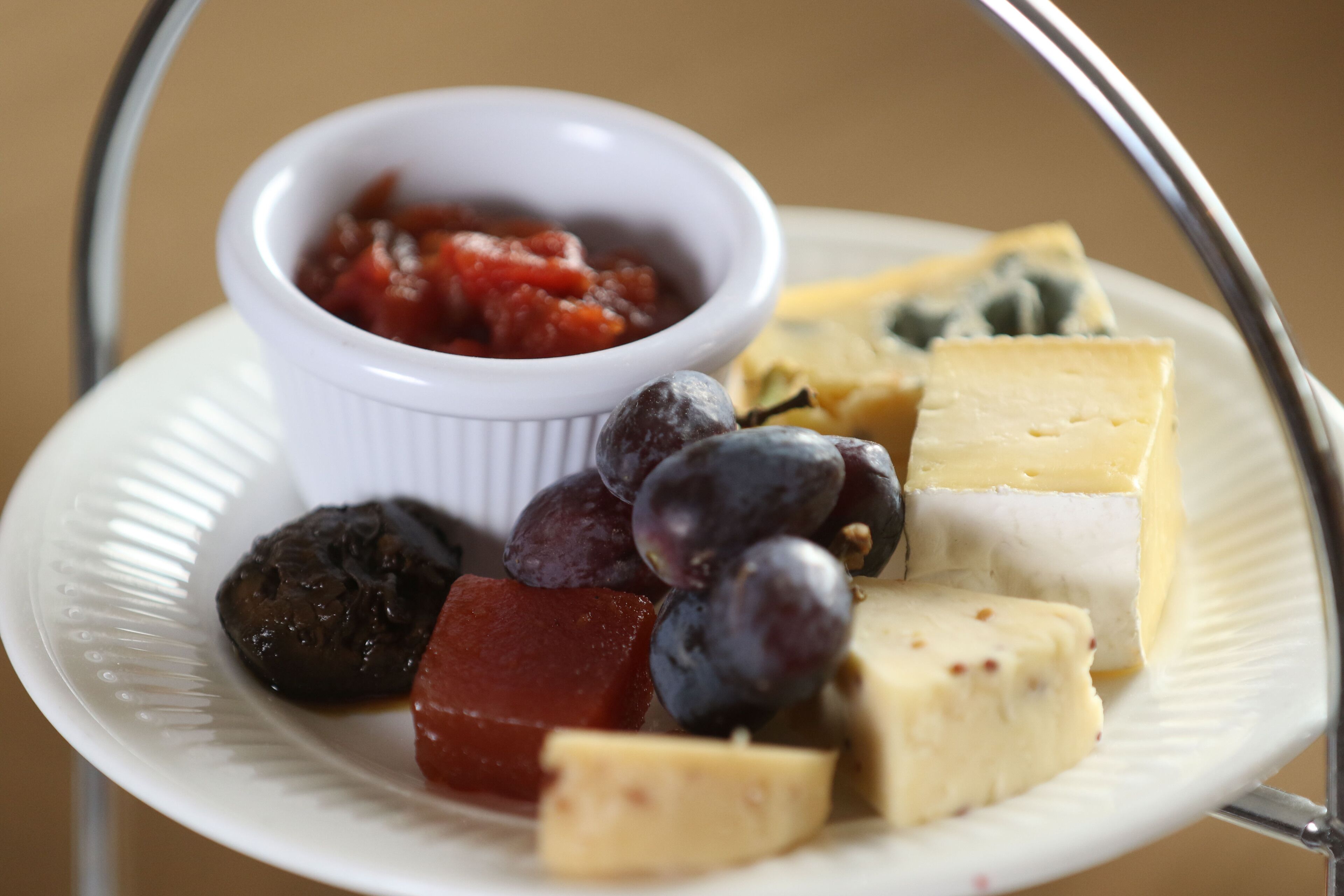 Un plato con varios quesos, uvas y un pequeño recipiente con salsa de tomate.