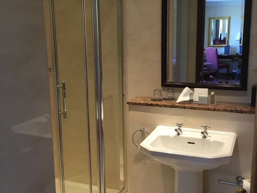 A modern bathroom with a glass shower enclosure, a white sink with a mirror above it, and a granite countertop.