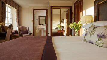 Habitación de hotel con una cama grande, un escritorio con silla, un tocador con espejo y una puerta que da a otra habitación.