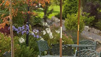 A garden patio with metal chairs and a table, surrounded by various plants and flowers.
