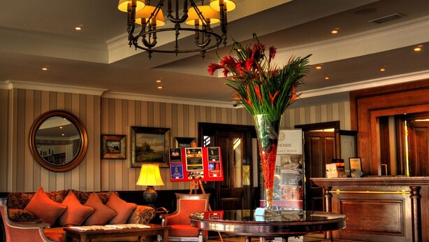 A lobby with a checkered floor, a sofa with red cushions, a table with a vase, a chandelier, and a reception desk. - Macdonald Drumossie Hotel (Inverness)