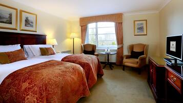 A hotel room with two beds, a desk, a chair, a TV, and a window with curtains.