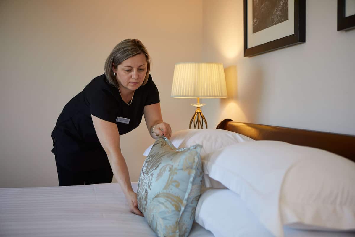 Hotellihuone, jossa on siististi pedattu sänky, yöpöytälamppu ja seinällä oleva kehystetty kuva.