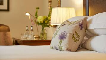 Habitación de hotel con una cama bien hecha, una mesita de noche con lámpara, un florero con flores y un cuadro en la pared.