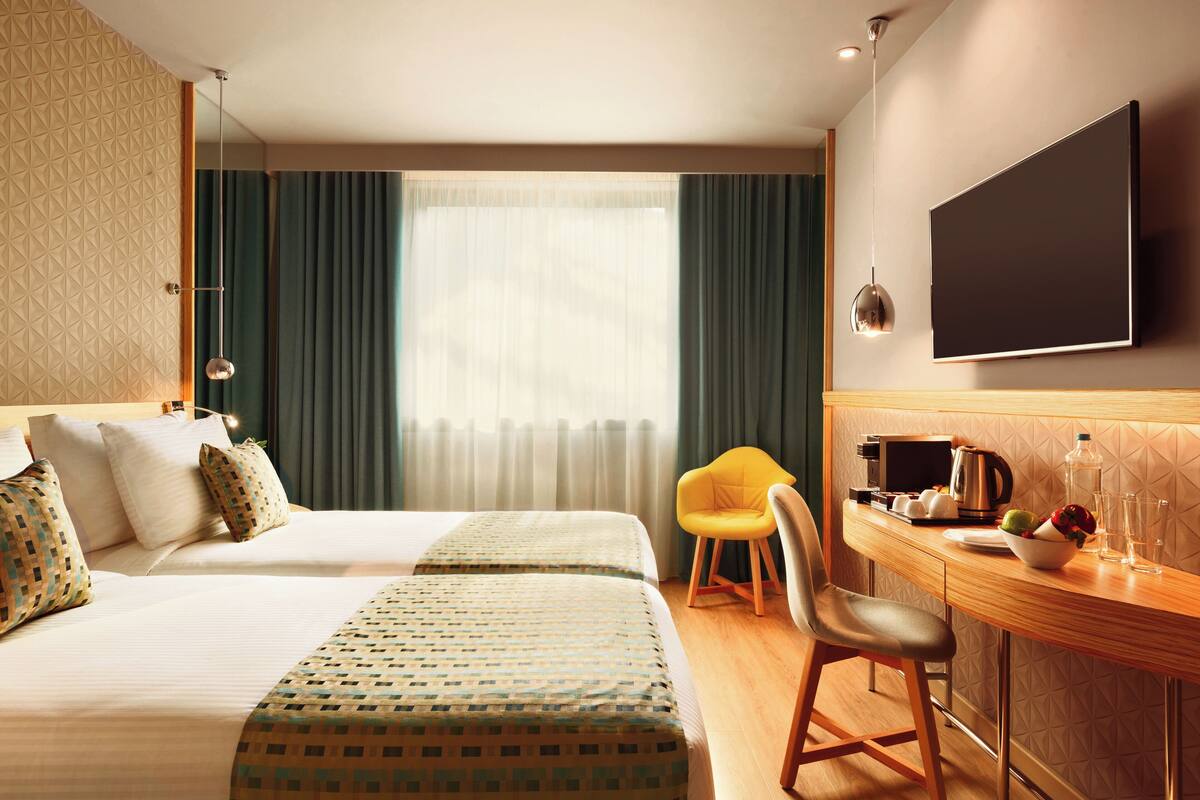 Una camera d'albergo con un letto, una scrivania con una sedia, una televisione e una finestra con tende.