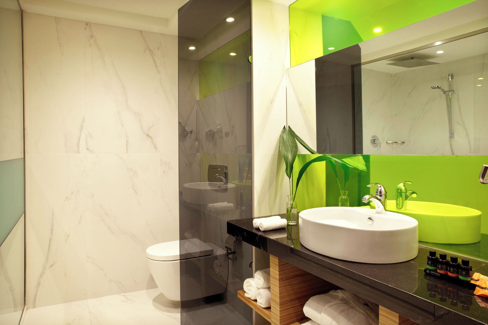 A modern bathroom with a marble floor, a white toilet, a black vanity with a white sink, and a green accent wall.