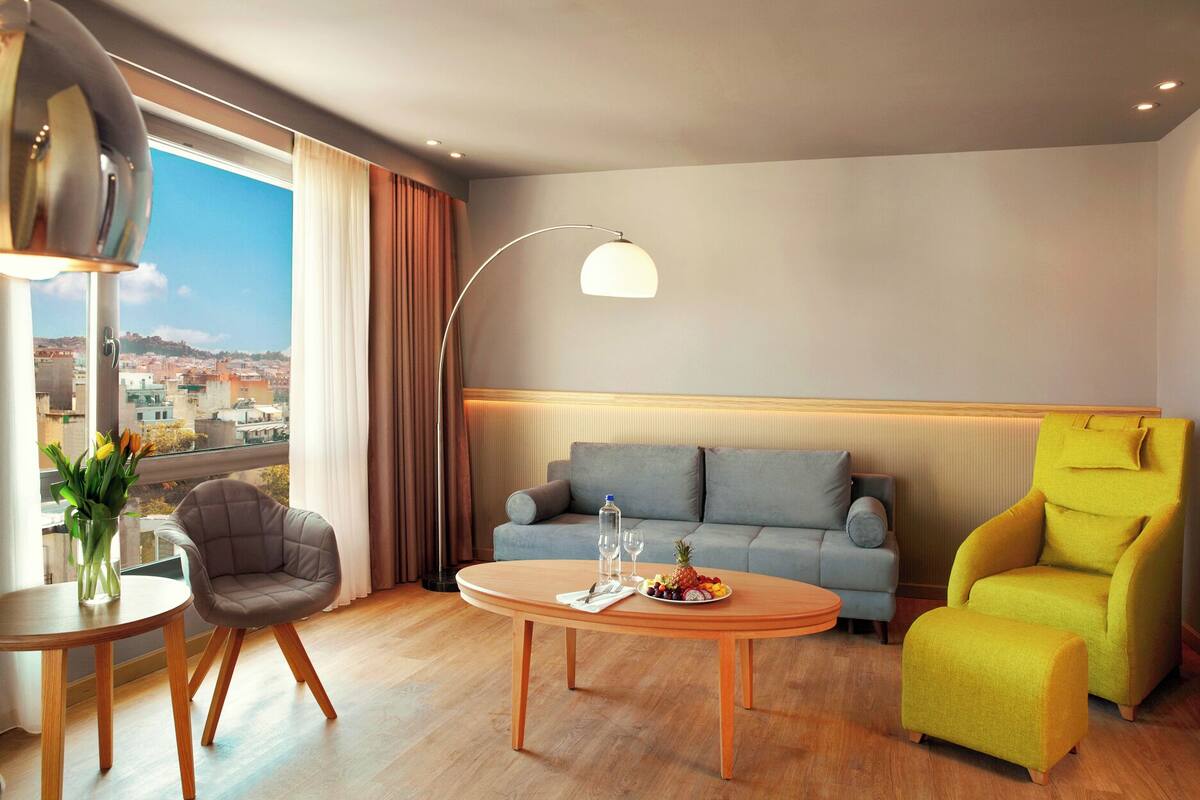Una camera d'albergo moderna con divano, poltrona e tavolino con un vassoio di frutta.