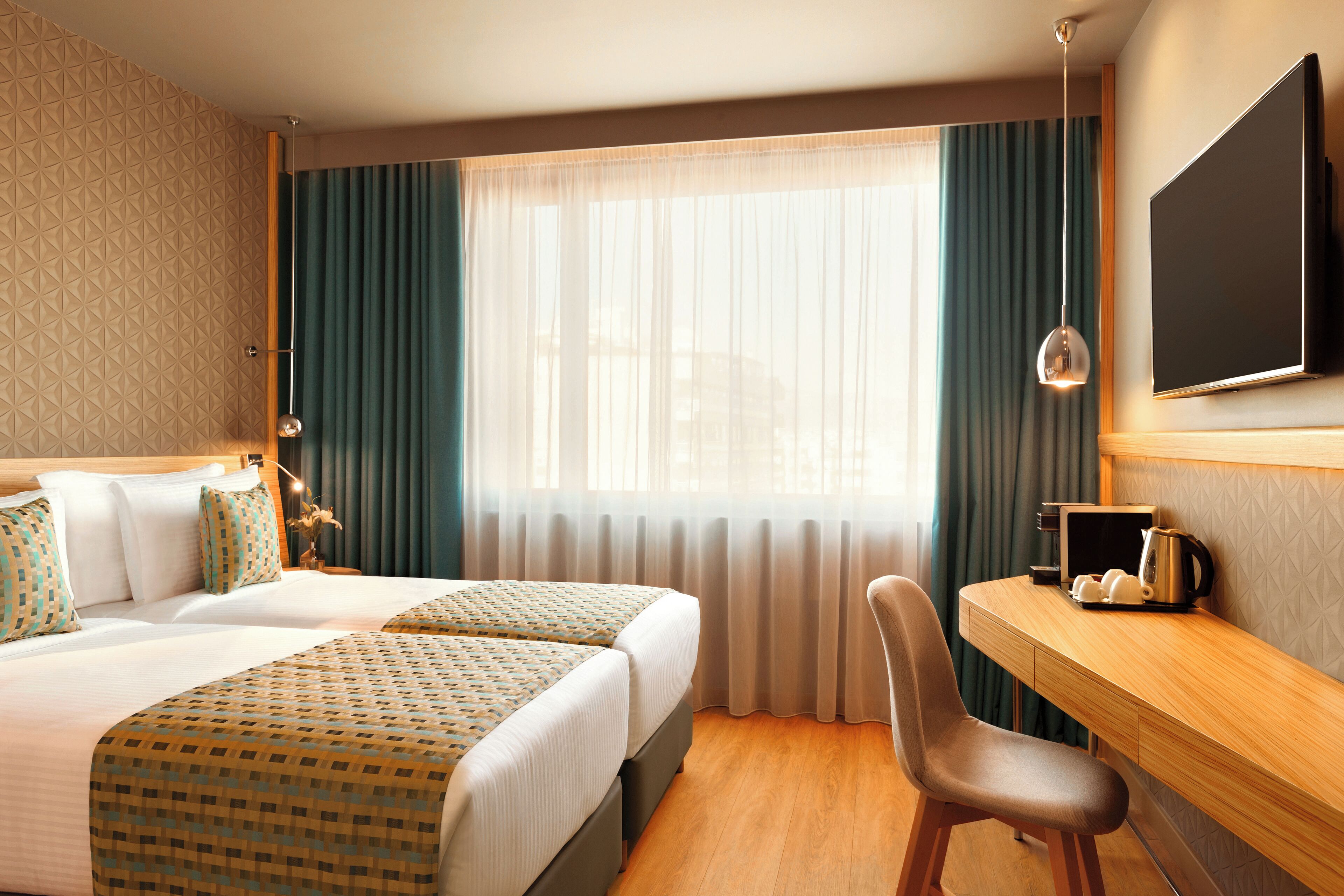 Une chambre d’hôtel avec deux lits, un bureau, une chaise, un téléviseur à écran plat et une fenêtre avec des rideaux.