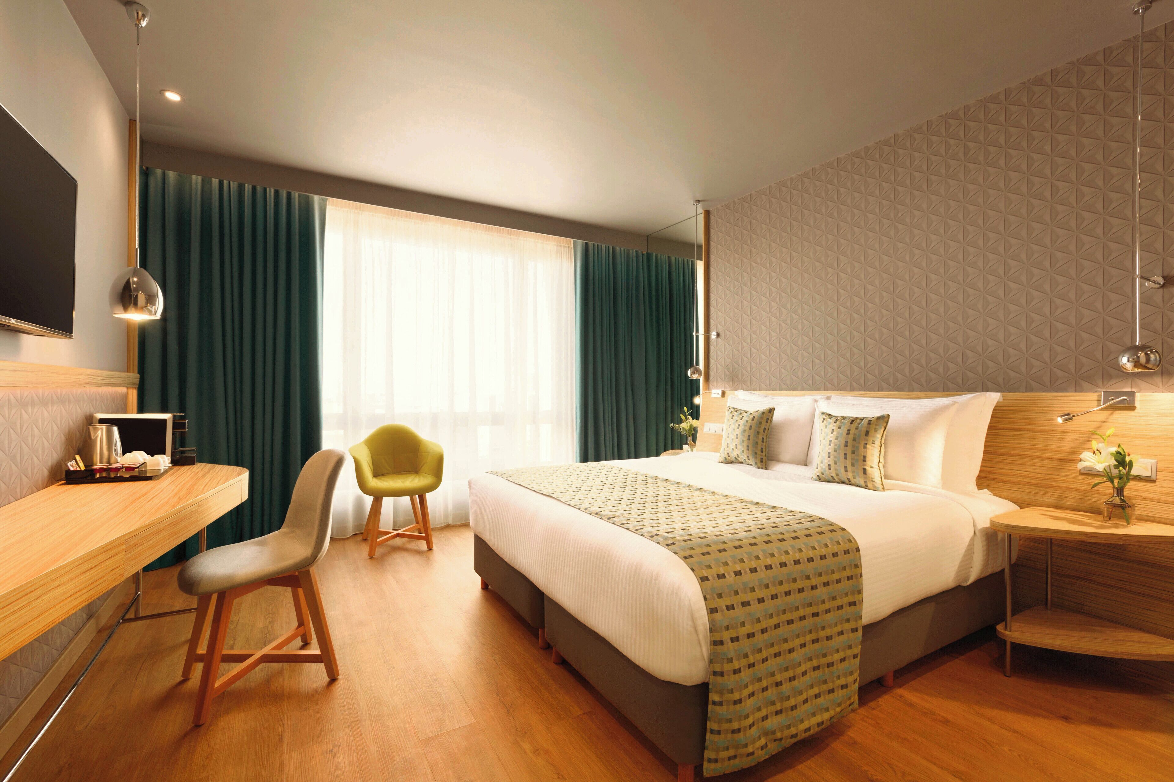 Una habitación de hotel con cama, escritorio, silla y mesita de noche con lámpara.