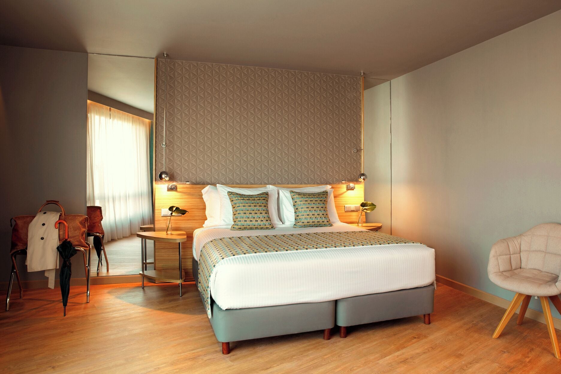 A modern hotel room with a large bed, two bedside tables, a chair, and a large window with curtains.